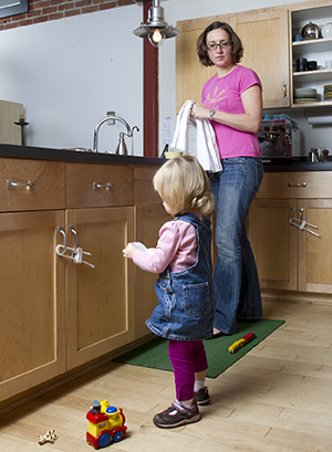 Mujer que observa a una niña pequeña que juega en la cocina. Los armarios tienen cierres de seguridad.