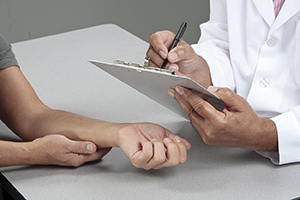 Proveedor de atención médica tomando notas mientras el paciente apoya su brazo sobre la mesa.