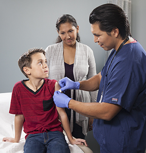 Proveedor de atención médica aplicando un inyección en el brazo a un niño mientras una mujer mira.