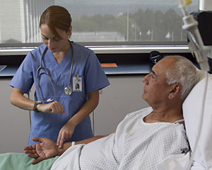 Proveedora de atención médica que revisa el pulso de un hombre que está en una cama de hospital.